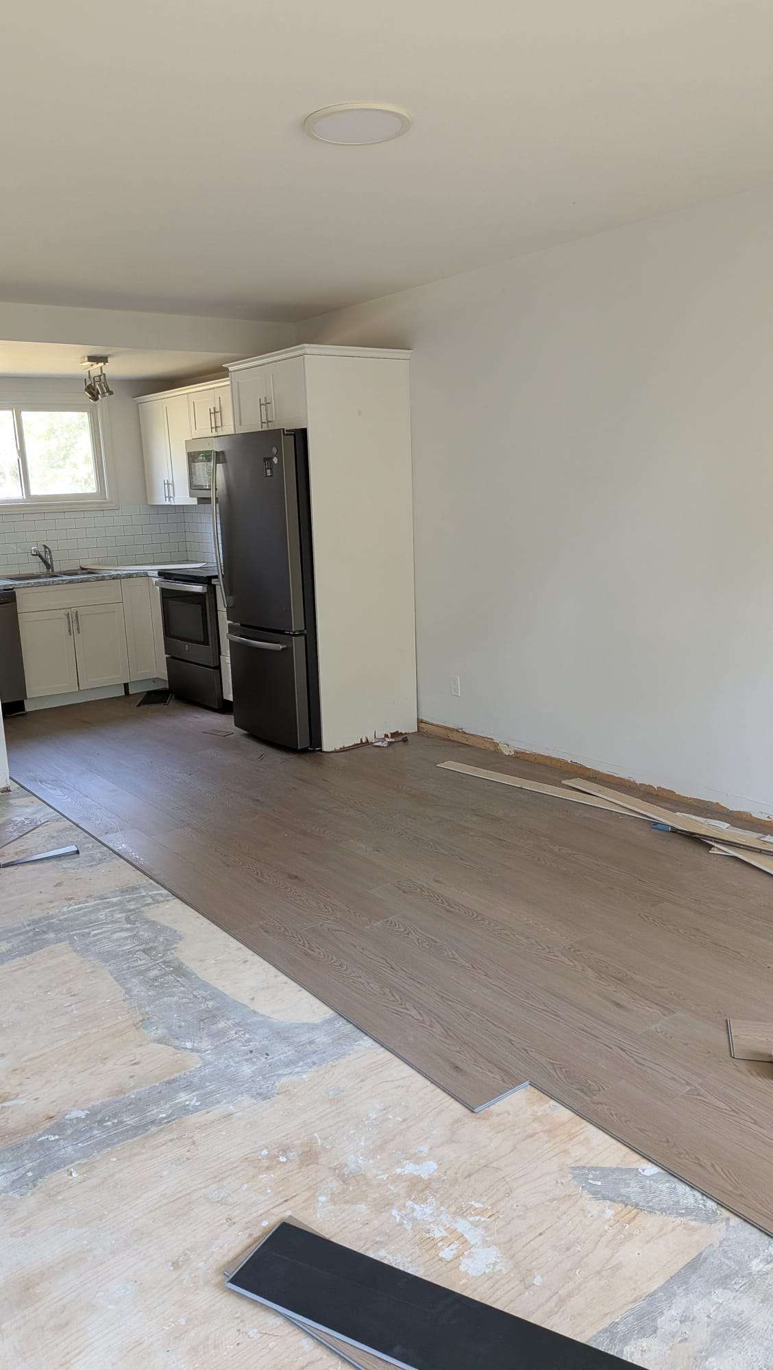 New flooring being installed beside a refrigerator in a bright kitchen